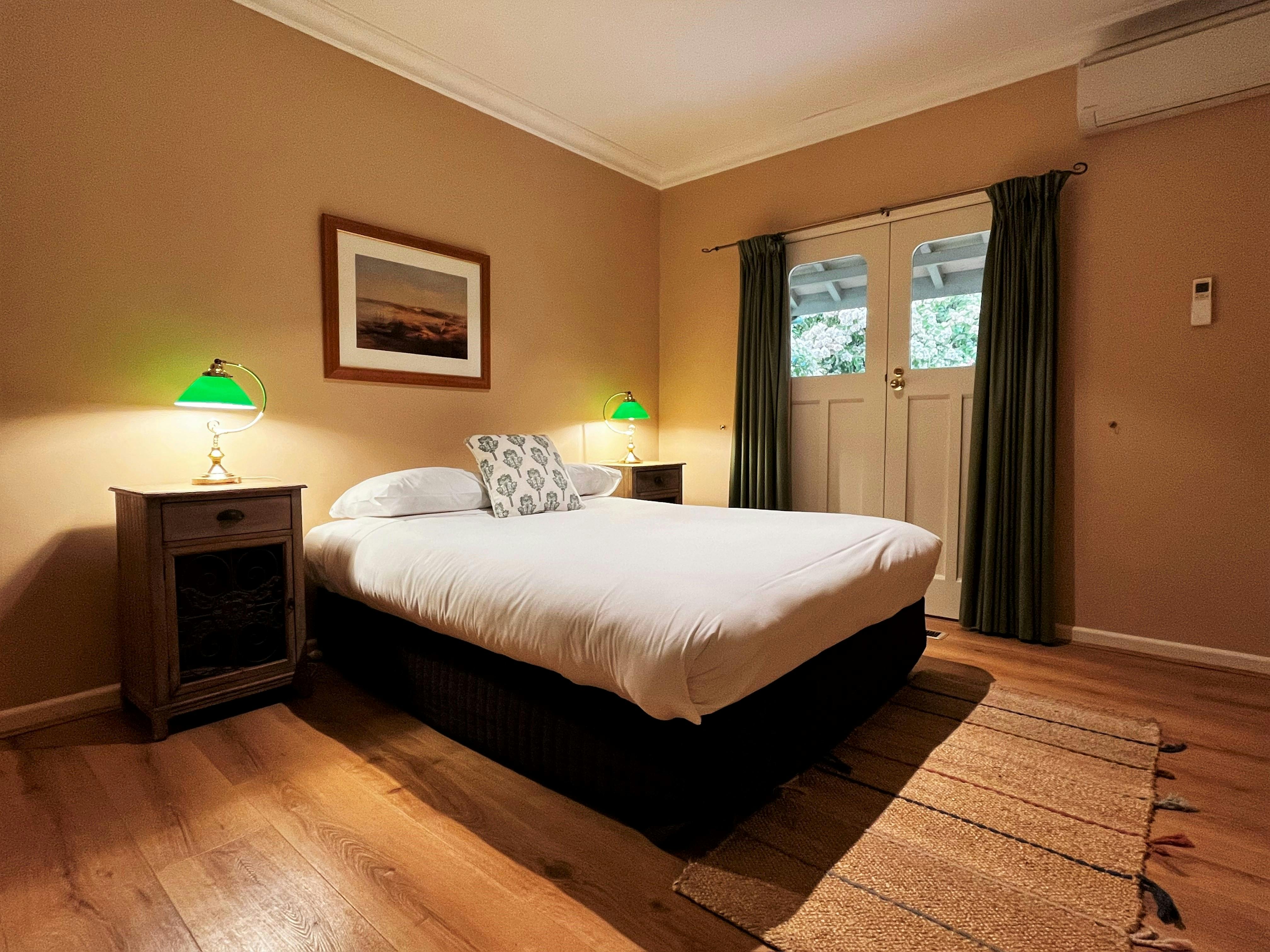 A warm bedroom with a cozy queen bed, vintage bedside lamps, and French doors to the verandah.