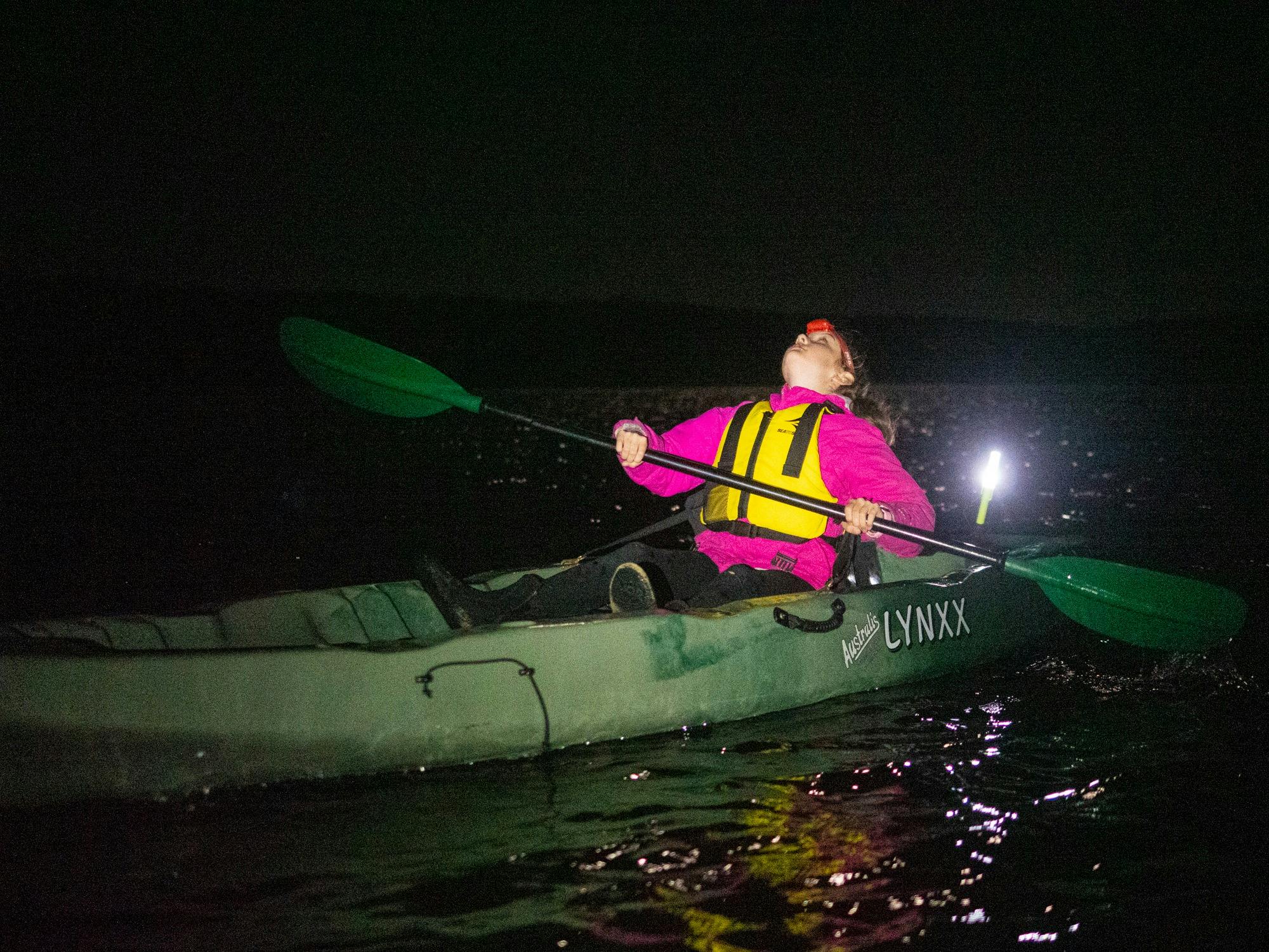 A young girl in a kayak at night, looking up at the sky filled with scattered stars