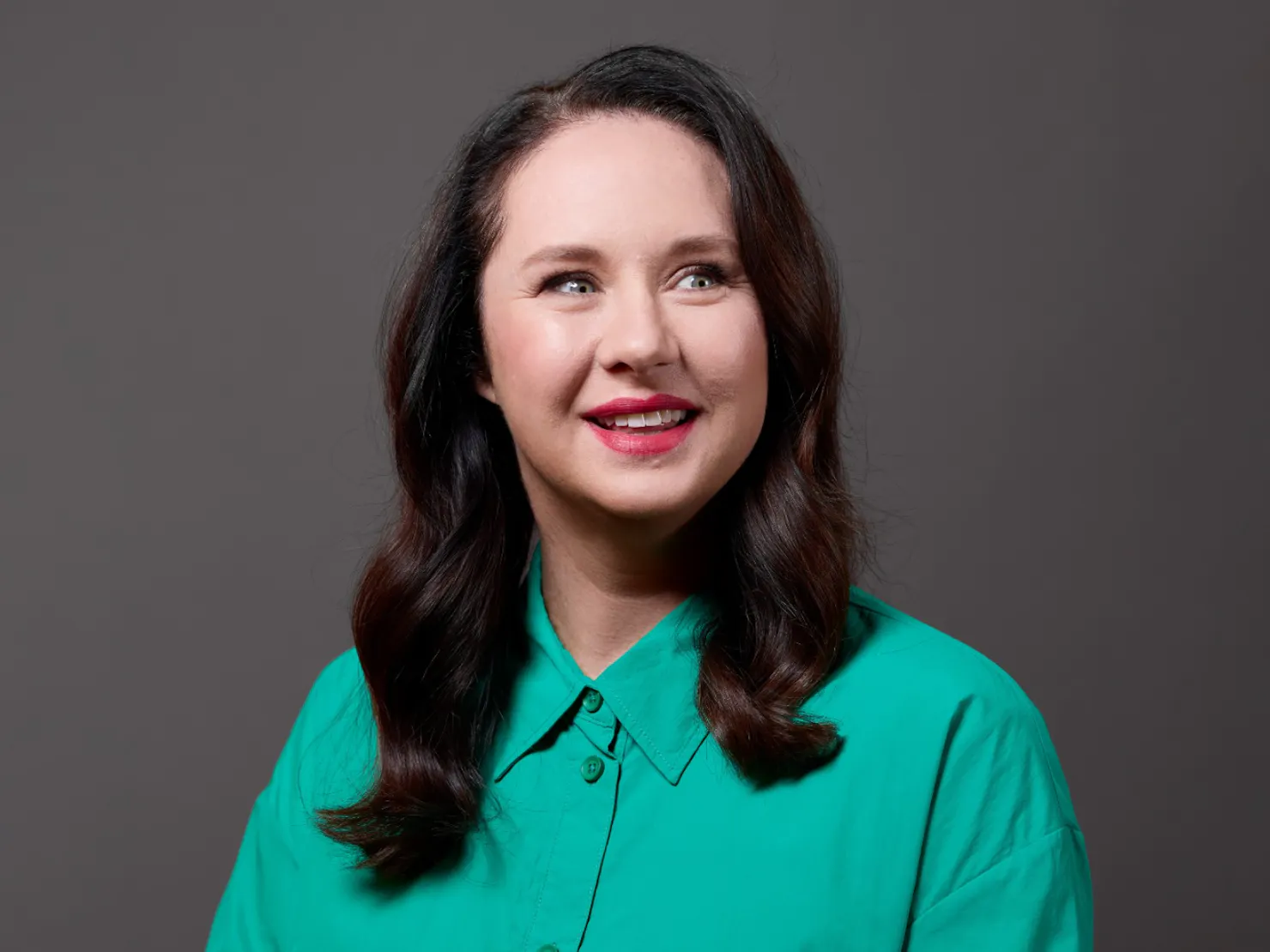 Middle aged women wearing a green shirt standing in front of a dark grey background.