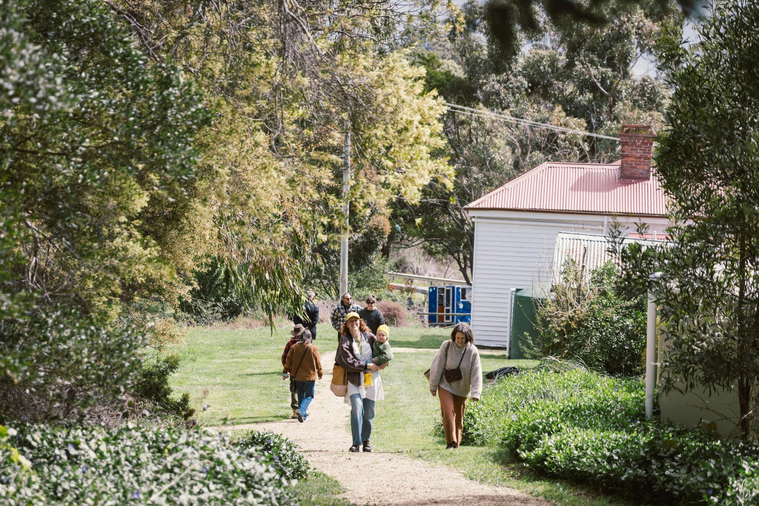 Several people are walking up a path amidst trees with an old building in the backtground.