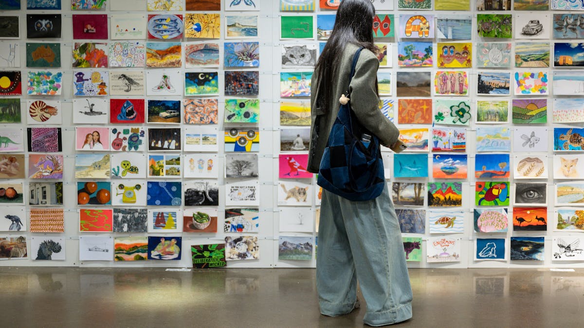 A person browsing A5 artworks displayed on a white wall at the Incognito Art Show.