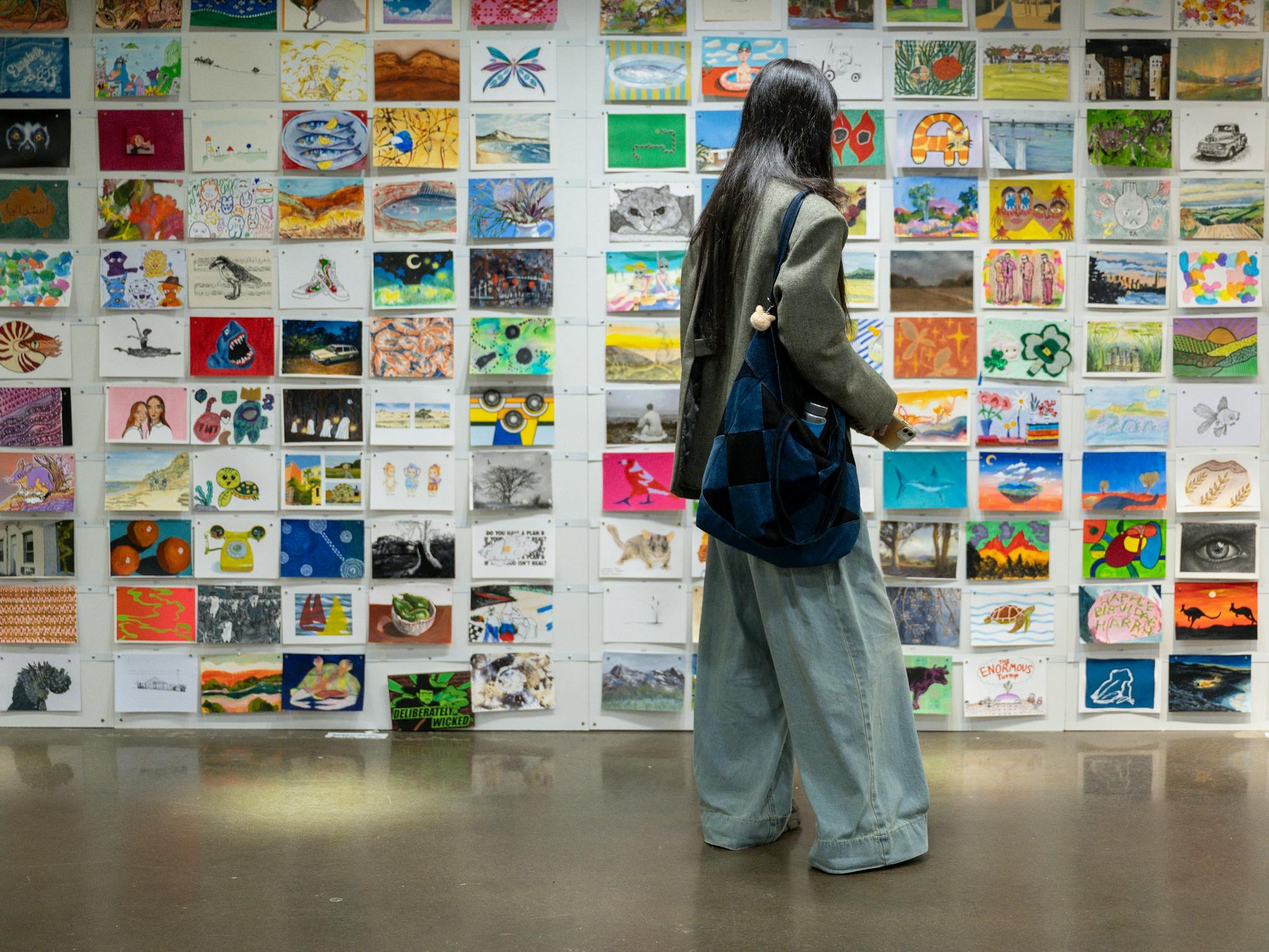 A person browsing A5 artworks displayed on a white wall at the Incognito Art Show. A person browsing A5 artworks displayed on a white wall at the Incognito Art Show.