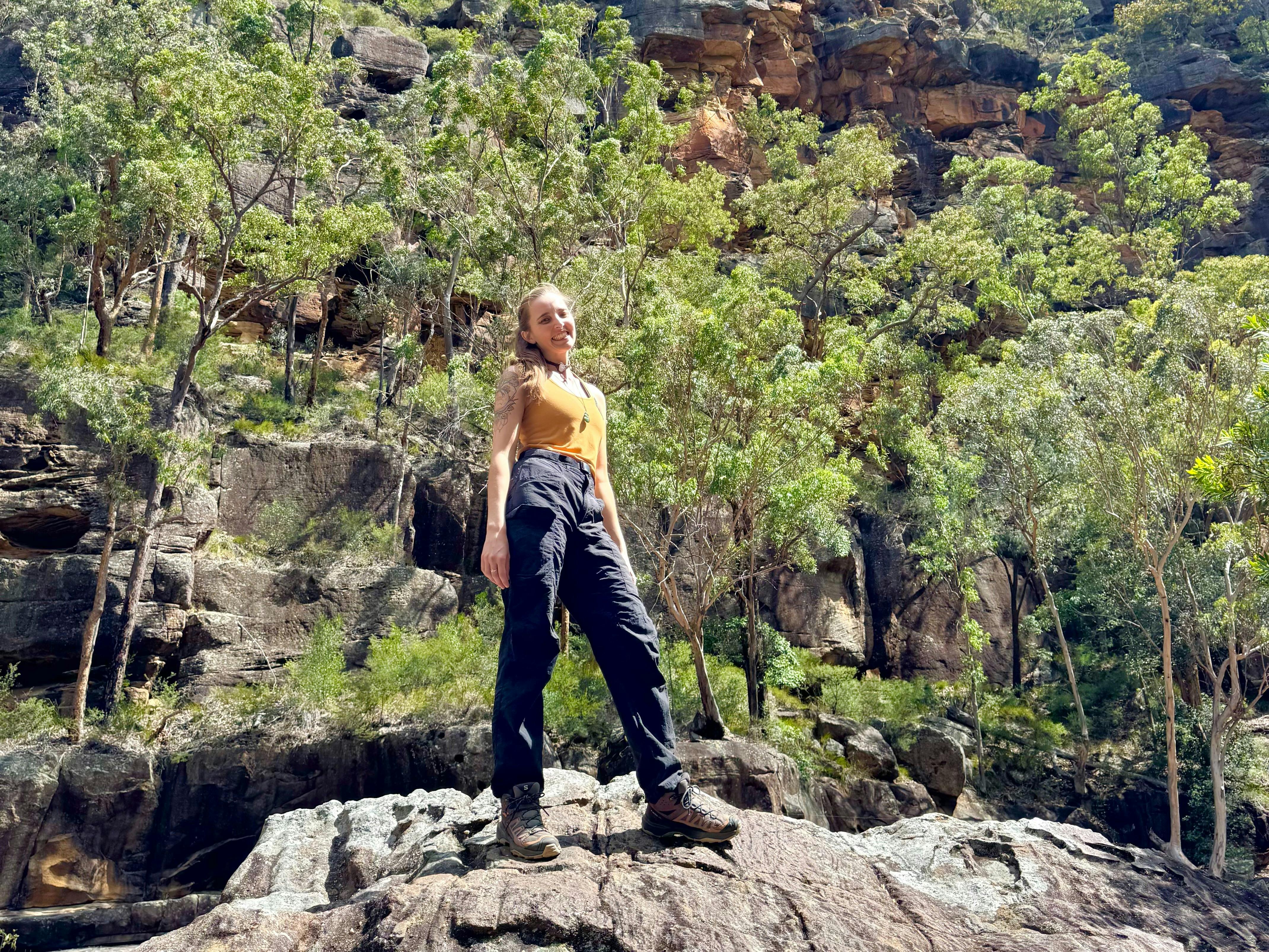 Die Führerin Caitlin steht auf einem Felsen vor hoch aufragenden Klippen und Eukalyptusbäumen.