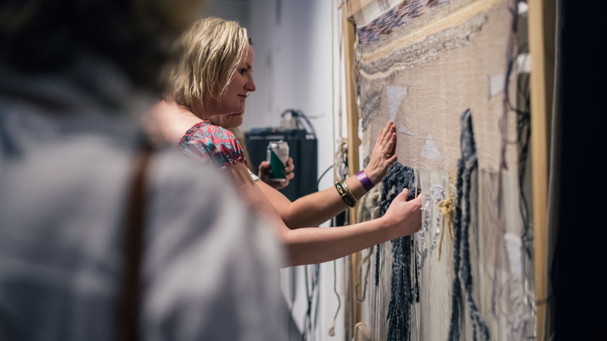Women touch the textile weaving on the gallery wall embedded with audio feedback and sound