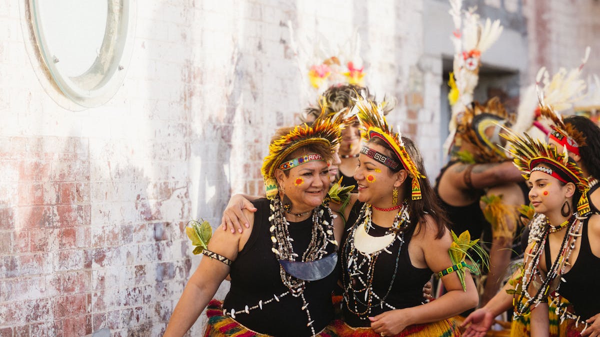 Two women in brightly coloured Papua New Guinea clothing walk with arms on each others shoulders