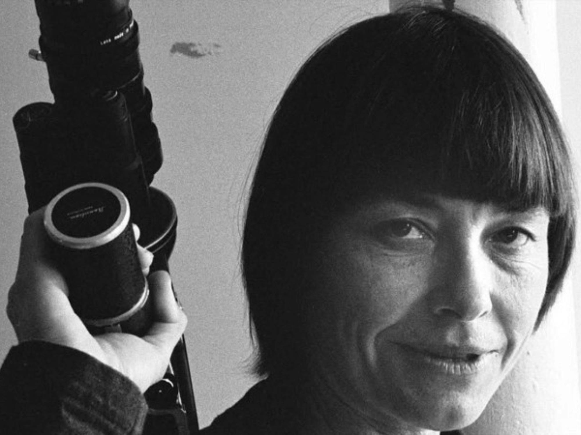 Black and white portrait of a woman with a dark bob holding a camera, looking straight at the camera