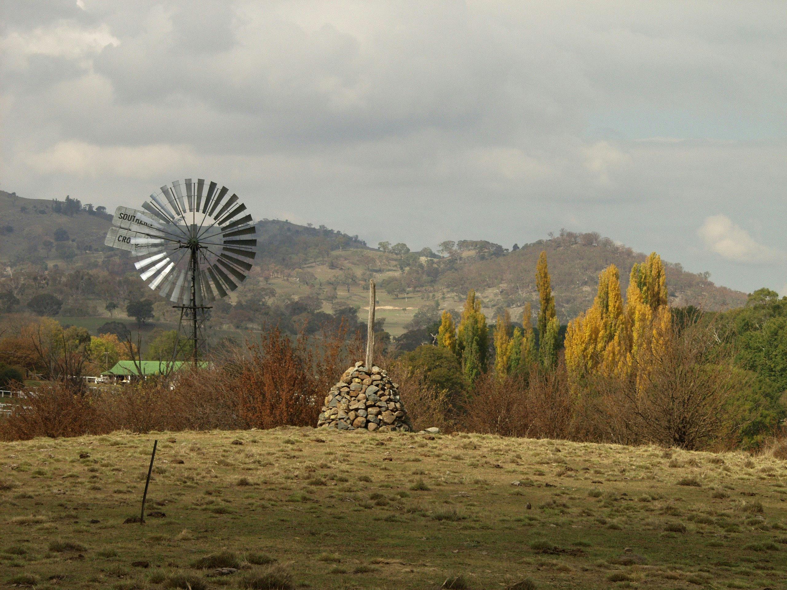Grassy foreground with stone cairn, windmill and poplars and homestead