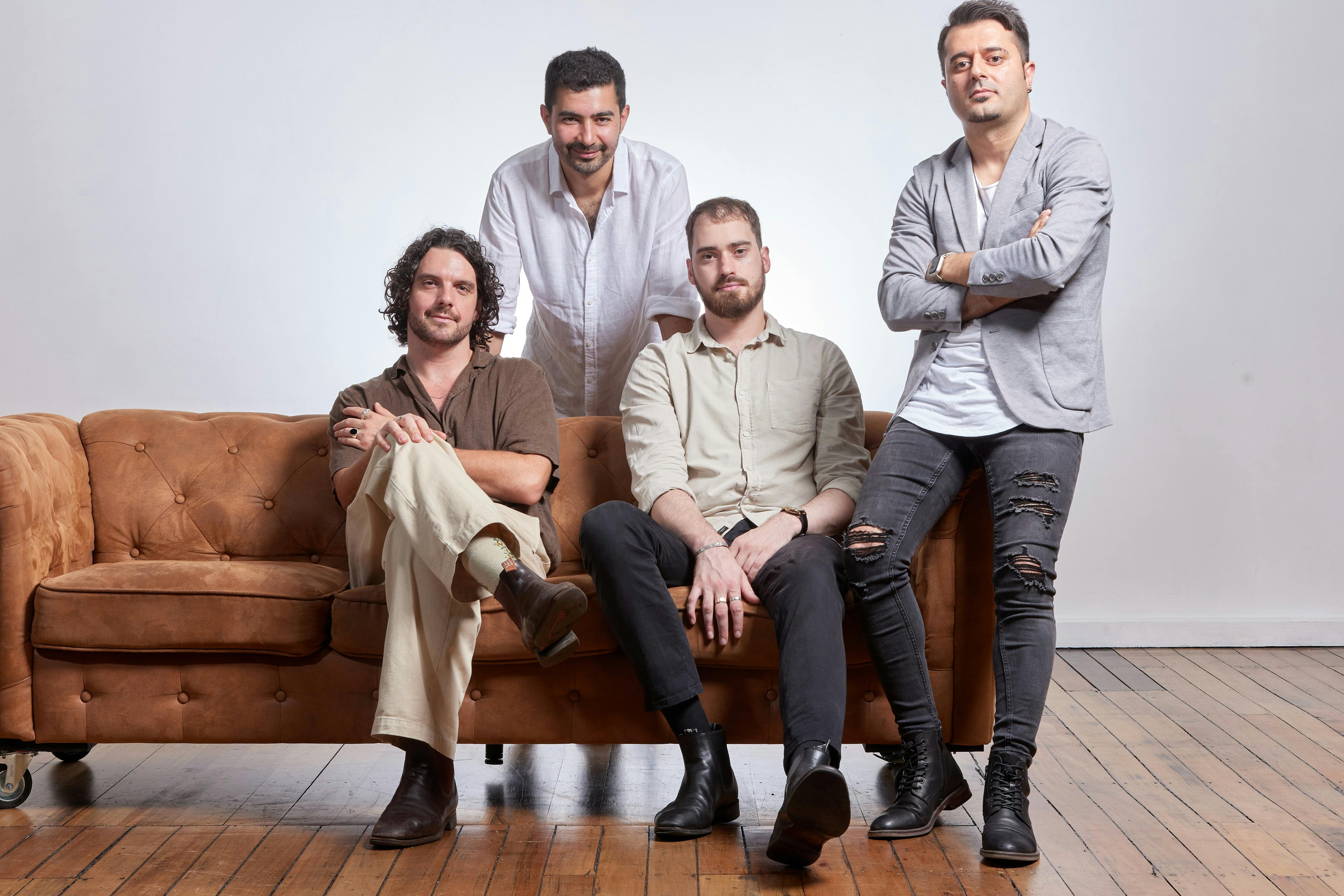 Two people seated on a brown couch, with two people leaning on the couch