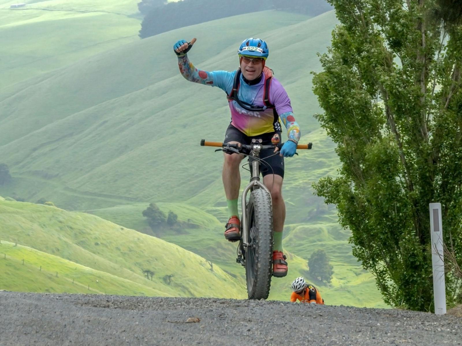 Rider in bright jersey fist pumps the air after climbing the gravel track on Mt Misery
