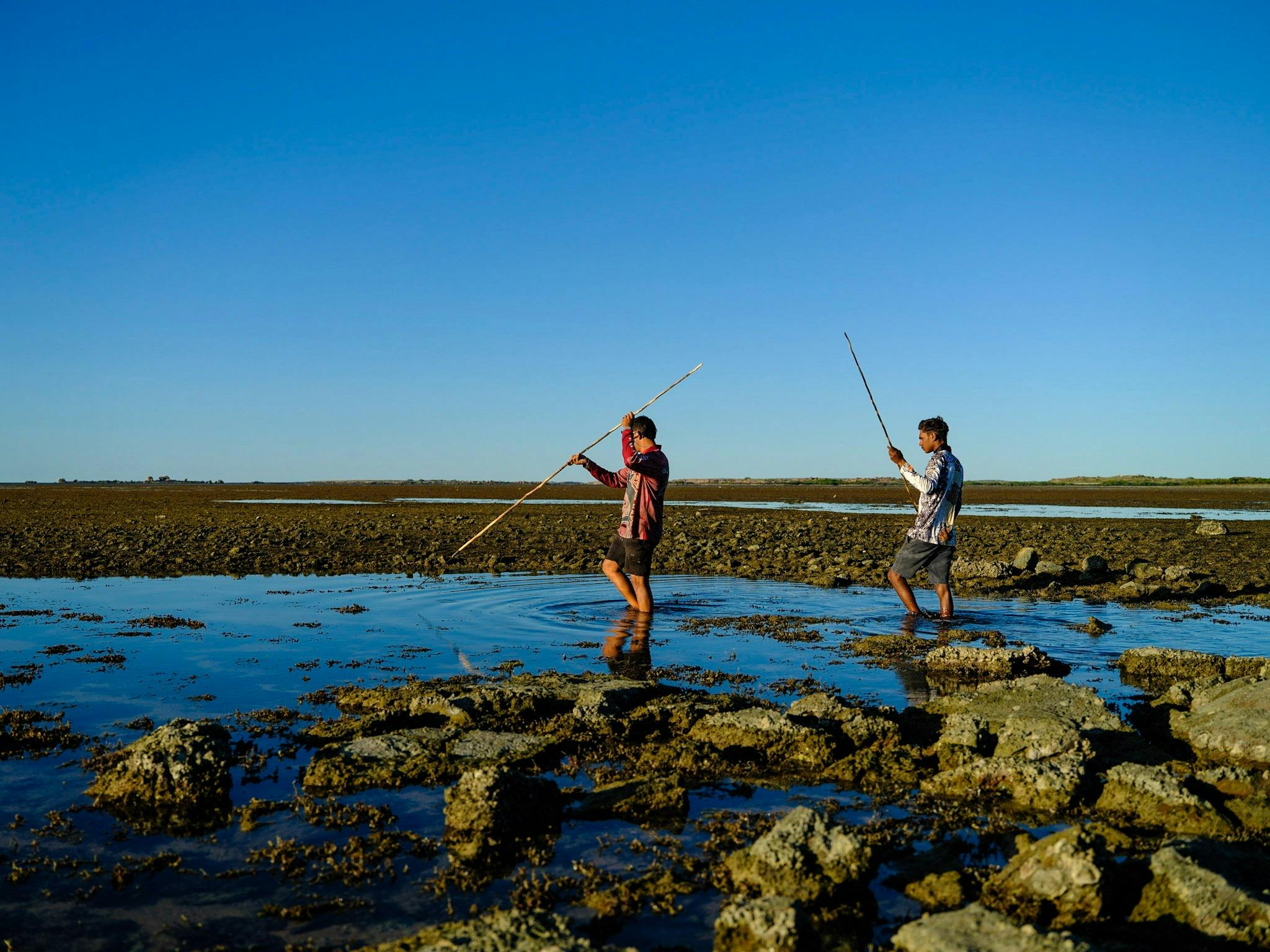 Two boys fishing with spears.