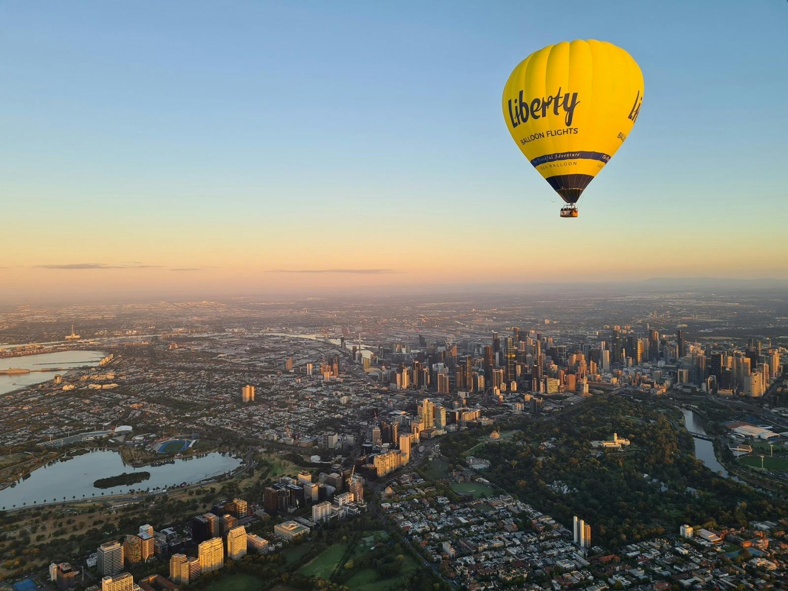 Yellow branded hot air balloon floating over Melbourne city skyline.