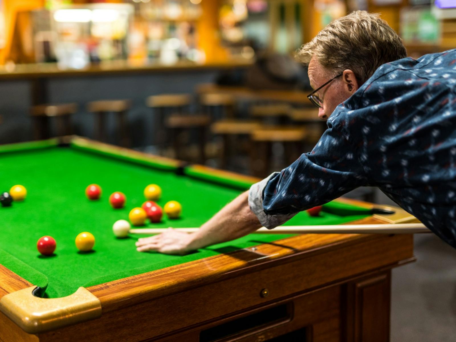 Man lining up a shot on a pool table with bar in background