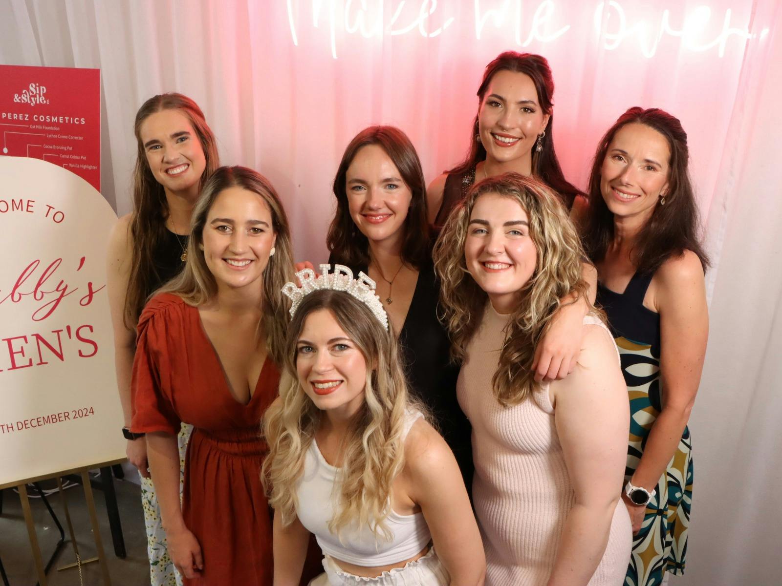 Bride-to-be posing with friends at a Sip & Style Co hens event in front of a pink neon backdrop.