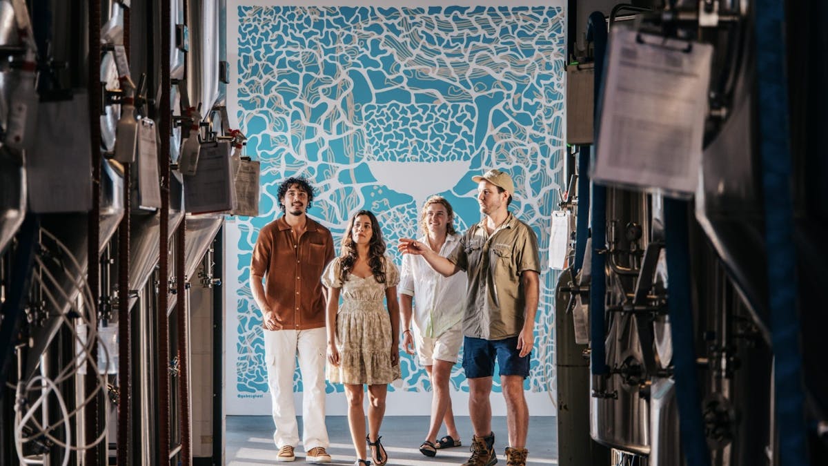 Four people framed by Stainless Steel tanks, in front of a blue and white background