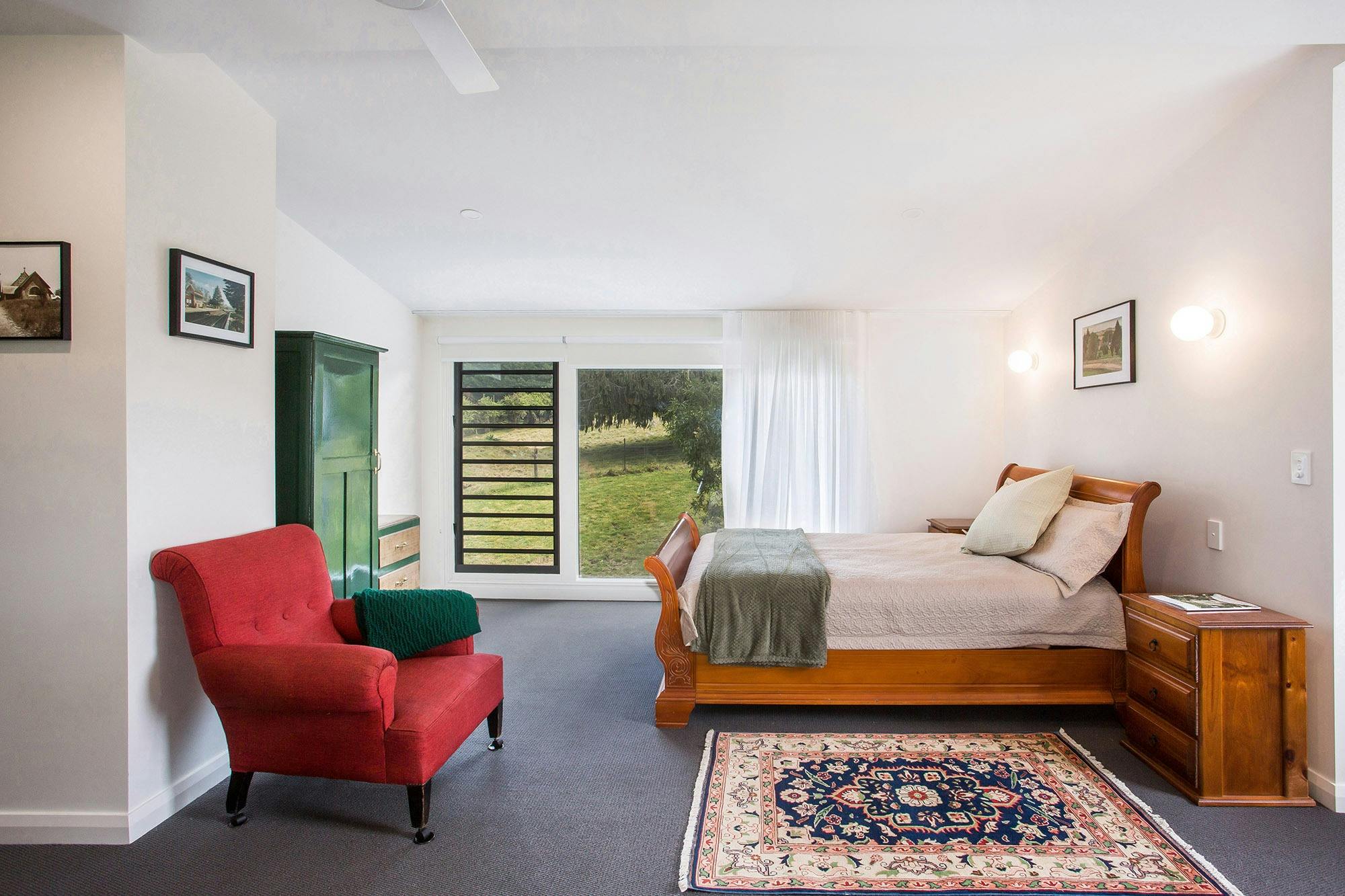 View of queen bed, chair, rug, wardrobe and picture window looking out to pastures