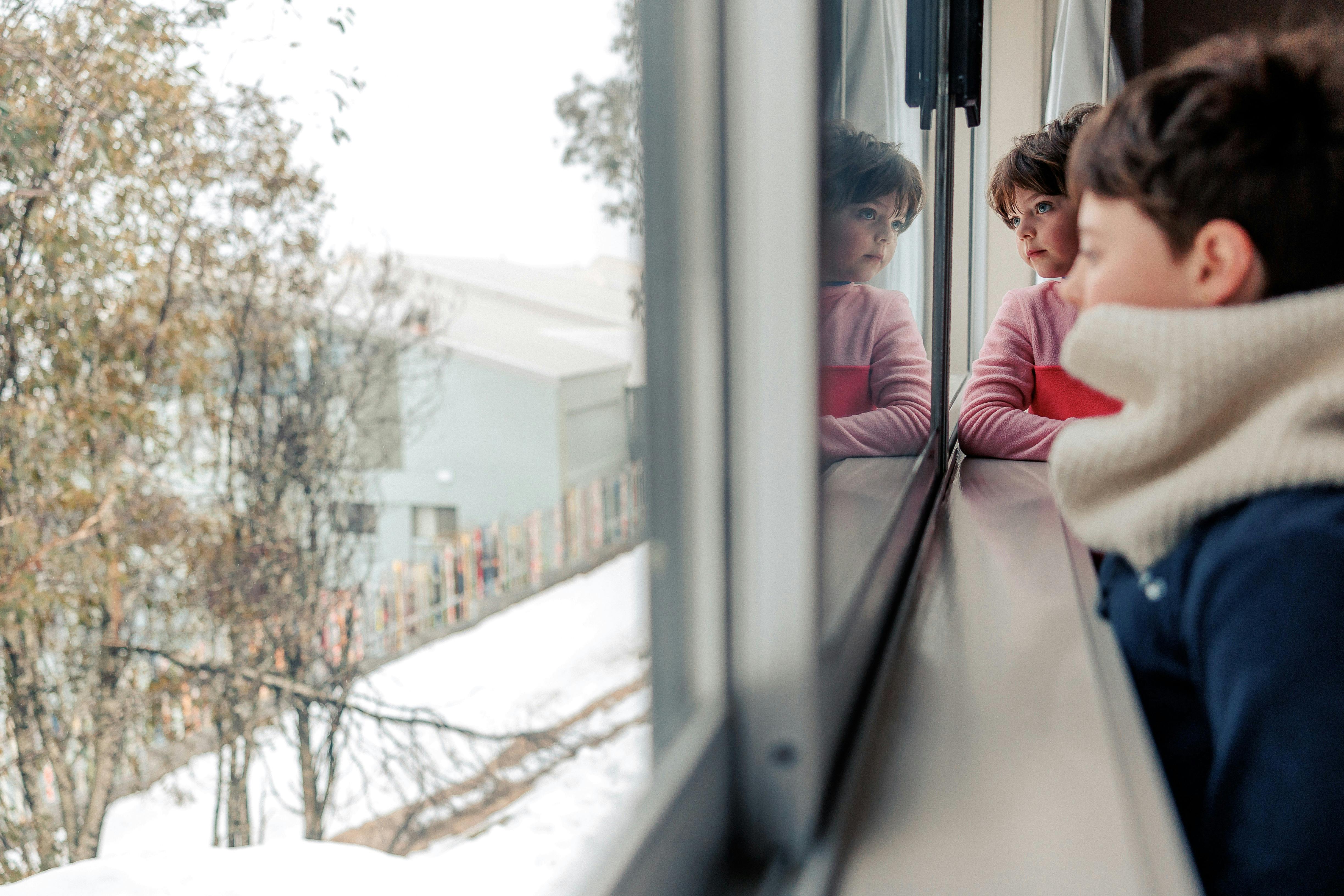 Two girls look out onto the snow from their room