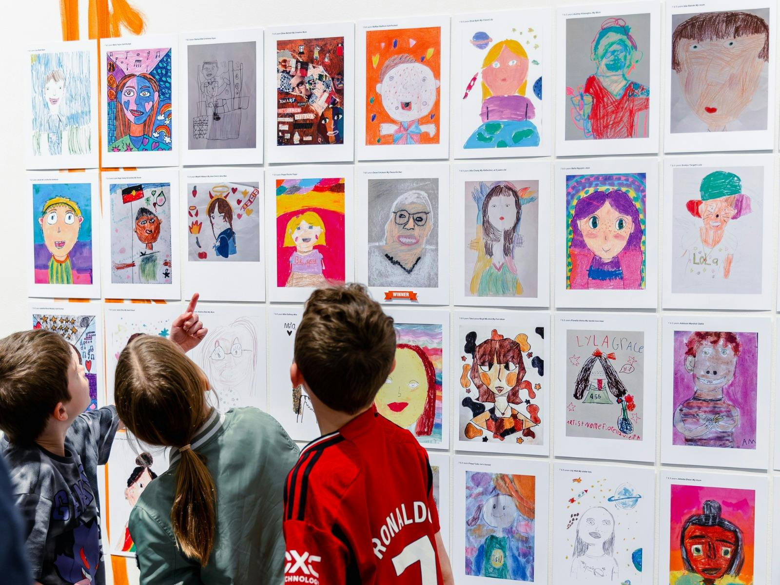 Young people looking at colourful artworks hanging on a gallery wall