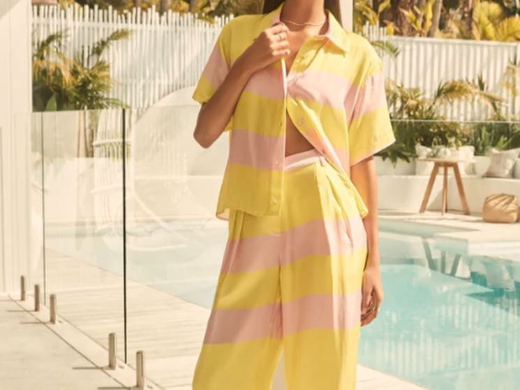 Model in a striped clothing  set. Sunny yellow and baby pink collared shirt and long pants.