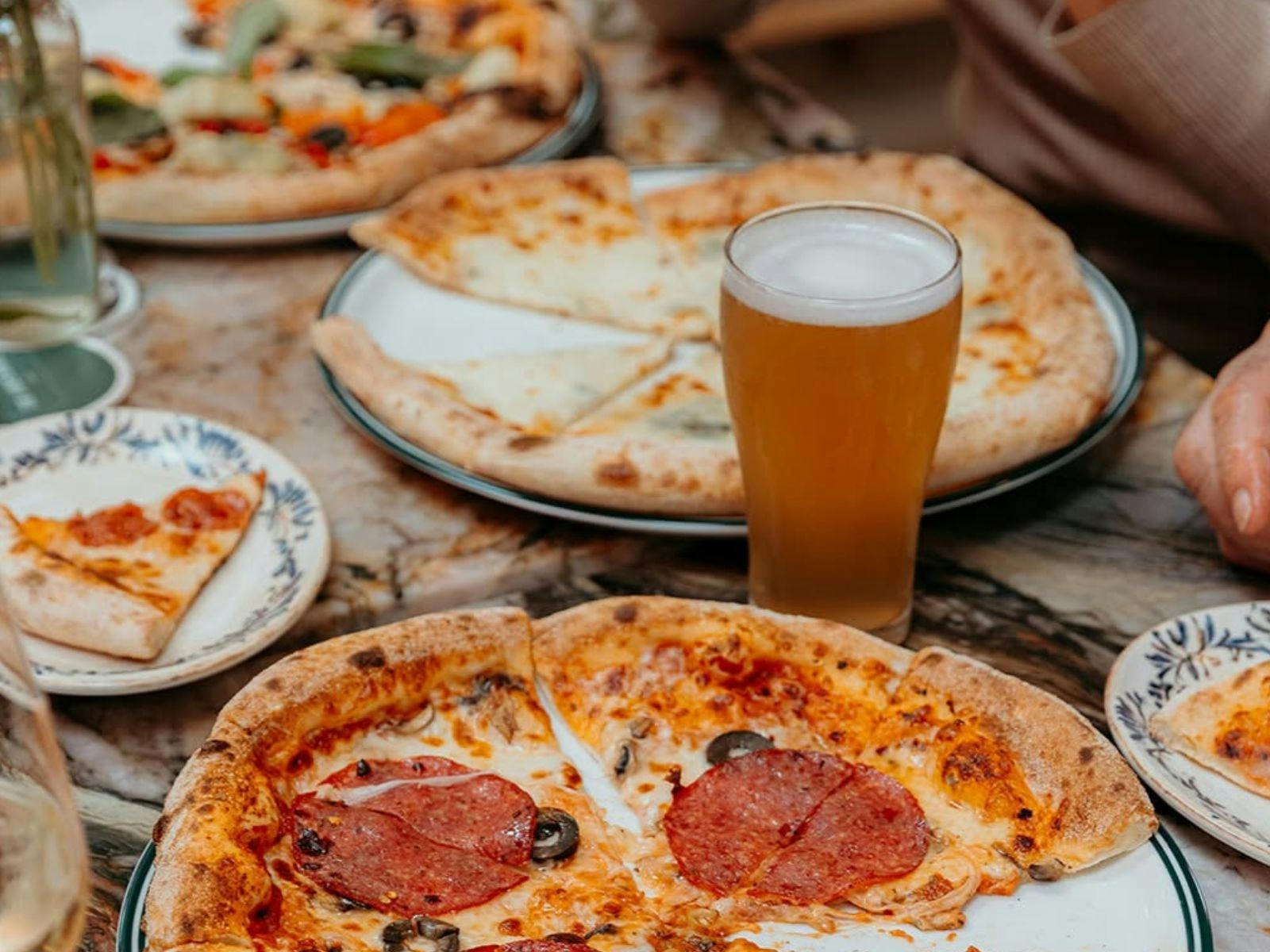different pizza varieties and beer on a table for people to enjoy
