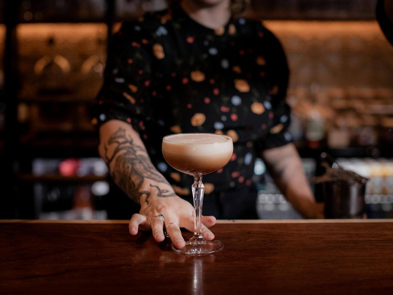 Espresso martini being held on bar by bartender with an octopus tattoo on their arm