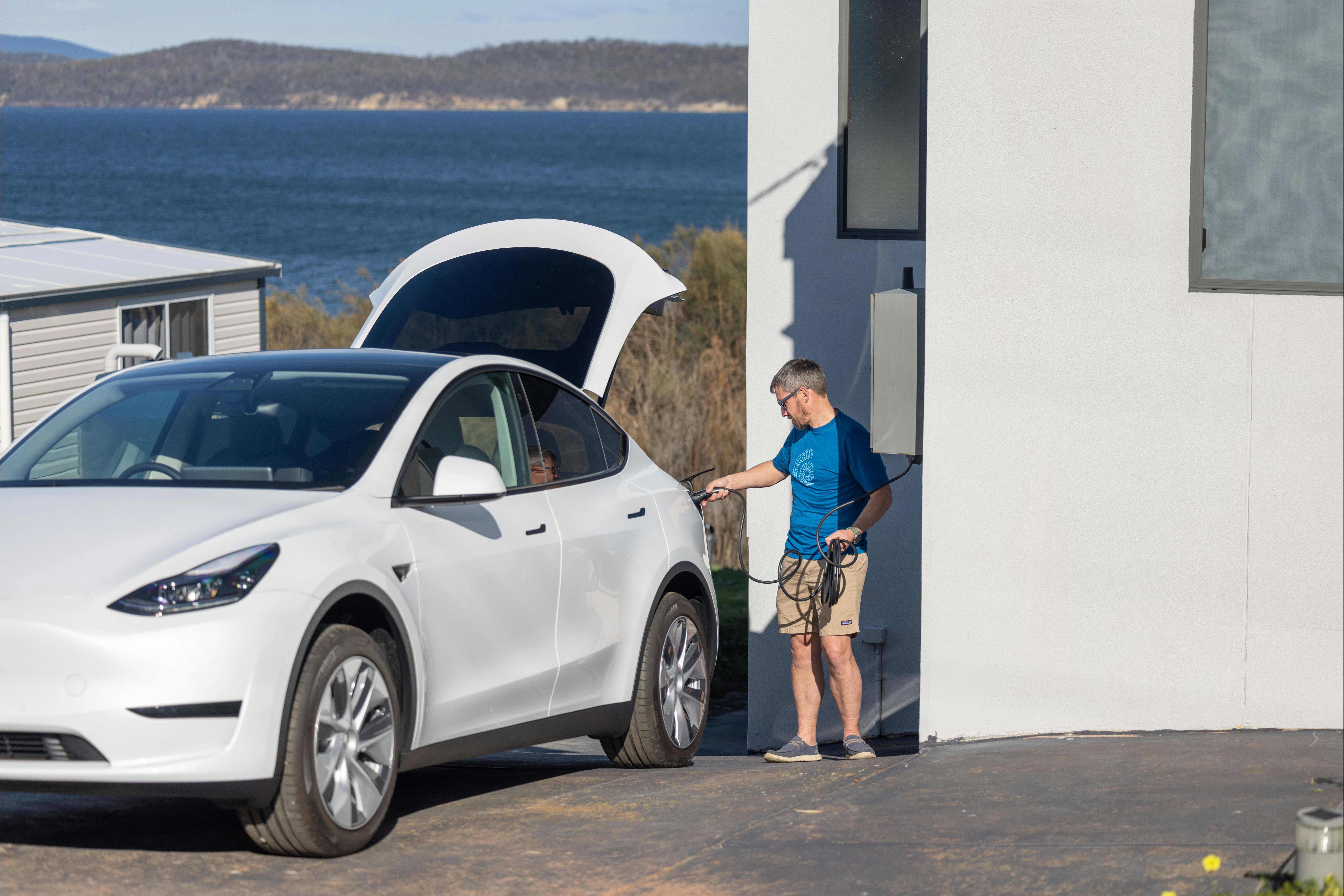 Electric vehicle (Tesla Model Y) being plugged in to charge by tourist at accommodation in Tasmania.