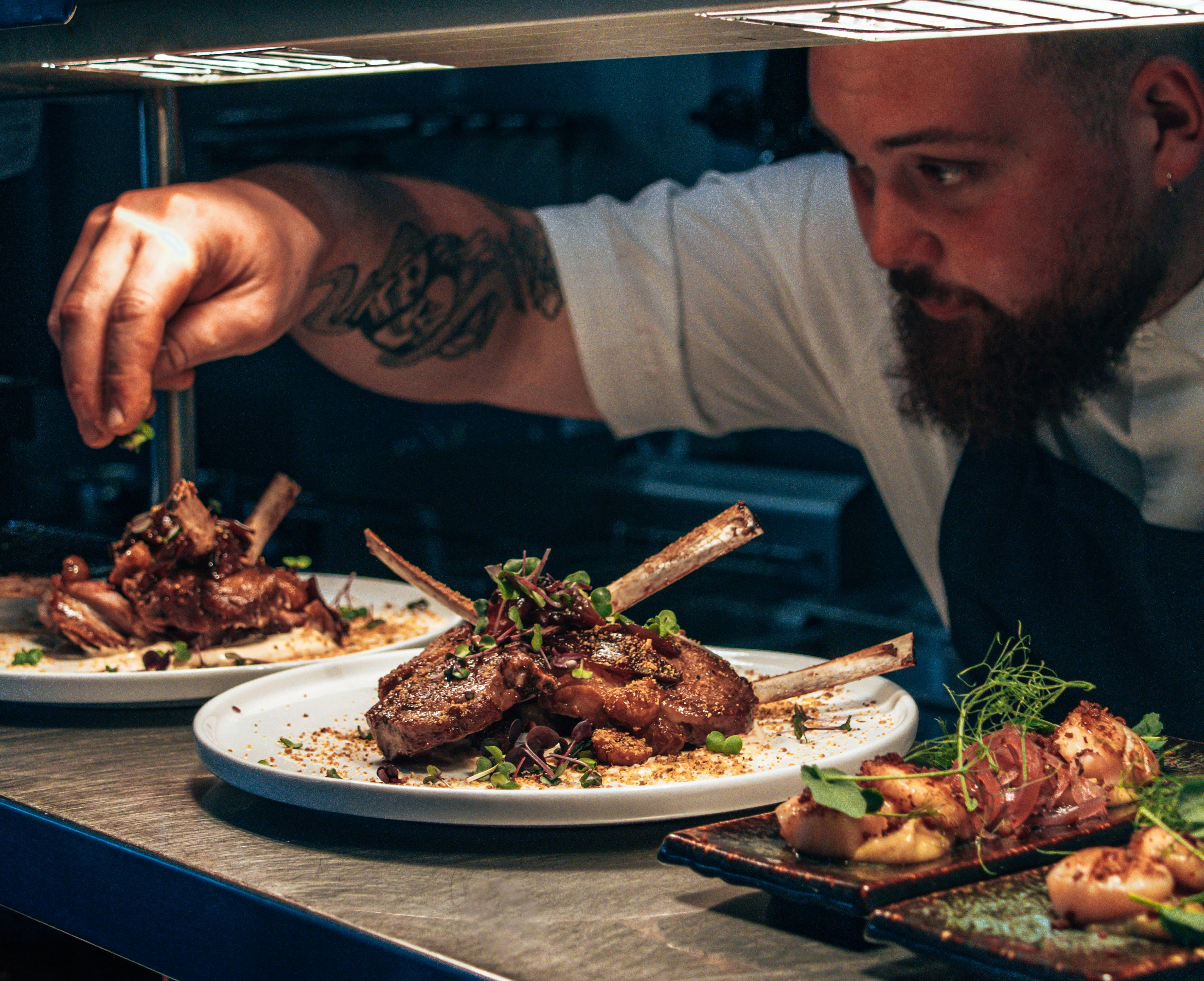 Chef sprinkling garnish on a dish of lamb