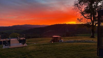 Sunset over rural countryside with mountain silhouettes and open grassy fields.