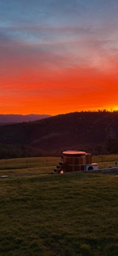 Sunset over rural countryside with mountain silhouettes and open grassy fields.