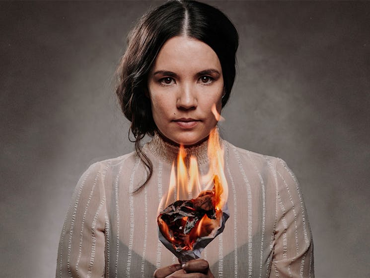Image of a young Jane Eyre (look-a-like) dressed in old attire, holding something on fire.