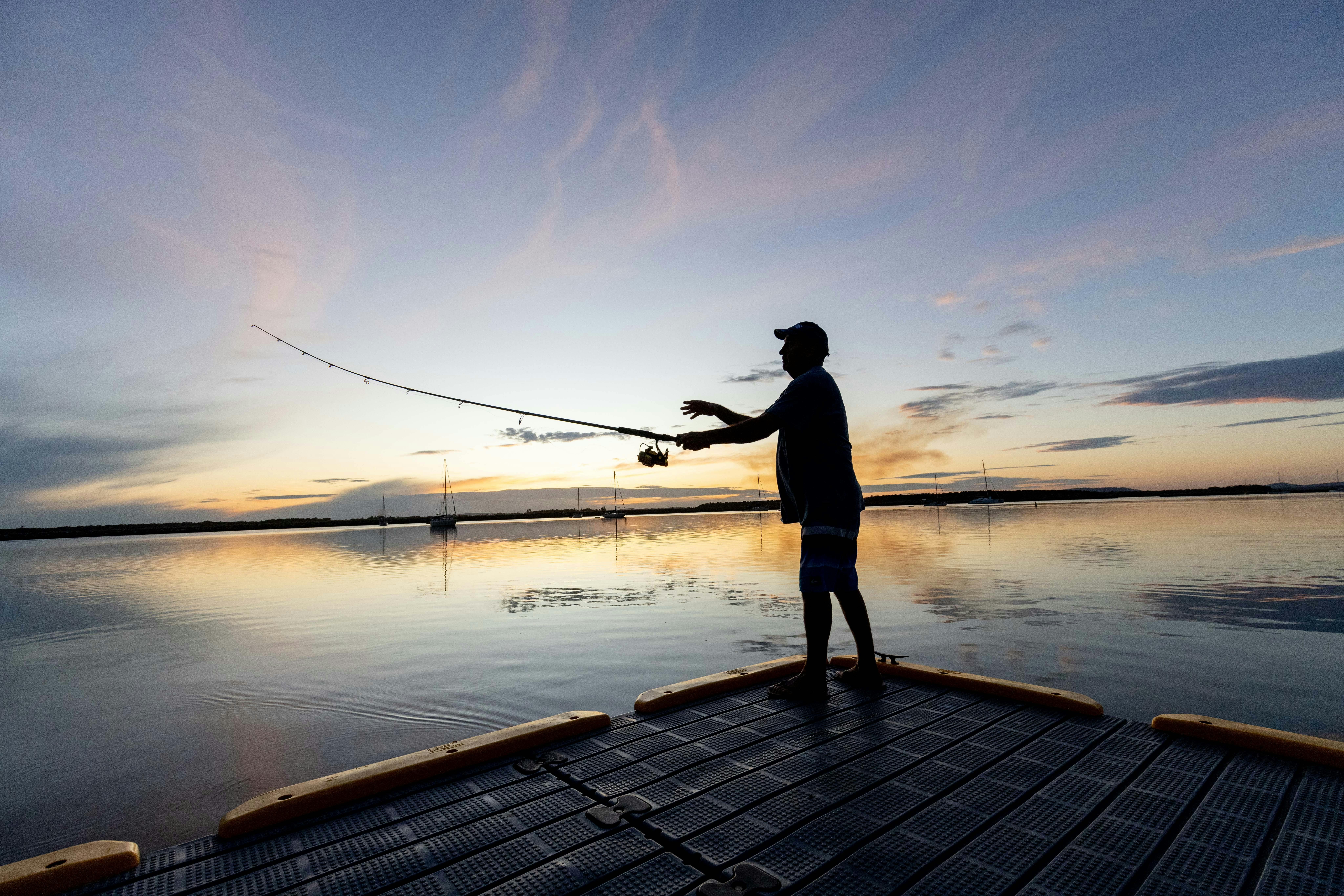 Ein Mann angelt bei Sonnenuntergang vom Steg aus.
