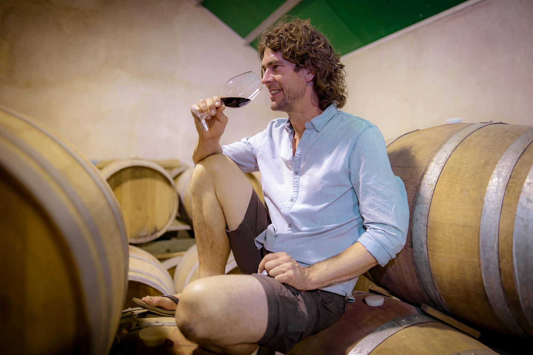 Winemaker tasting wine sitting on a barrel in a relaxed position