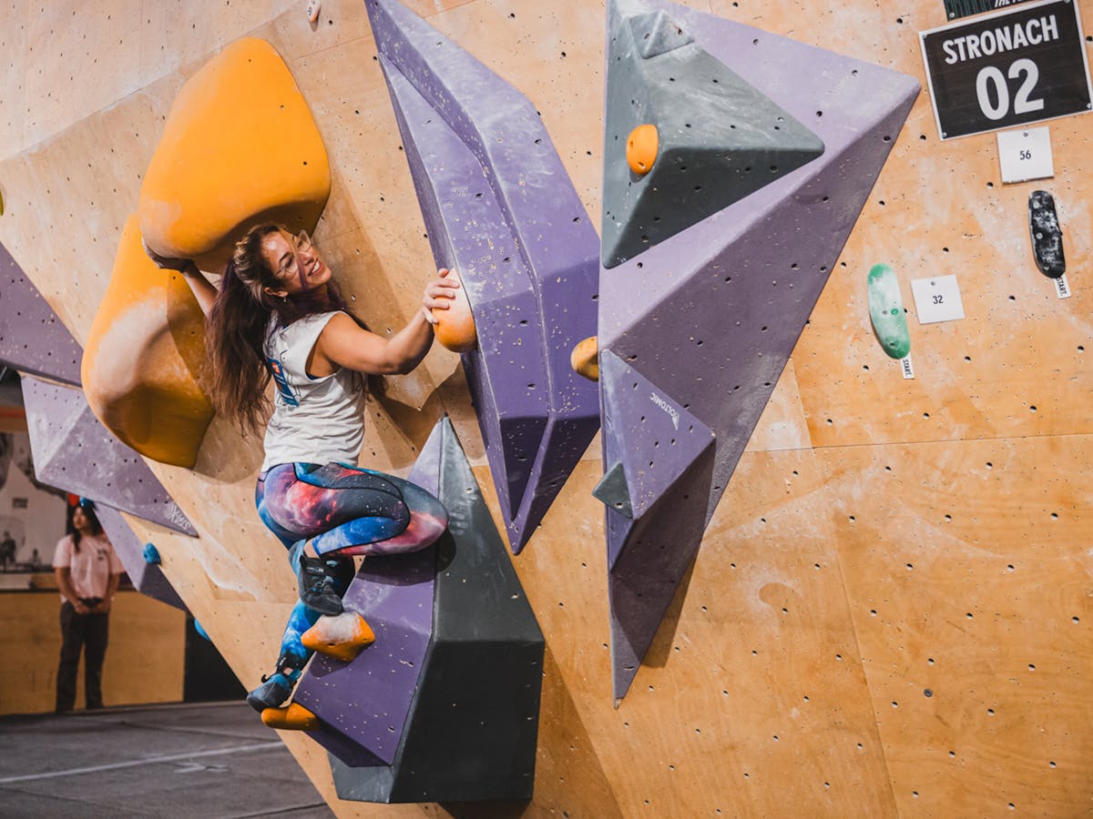 A climber navigating through a roof climb, purple triangle features and orange holds