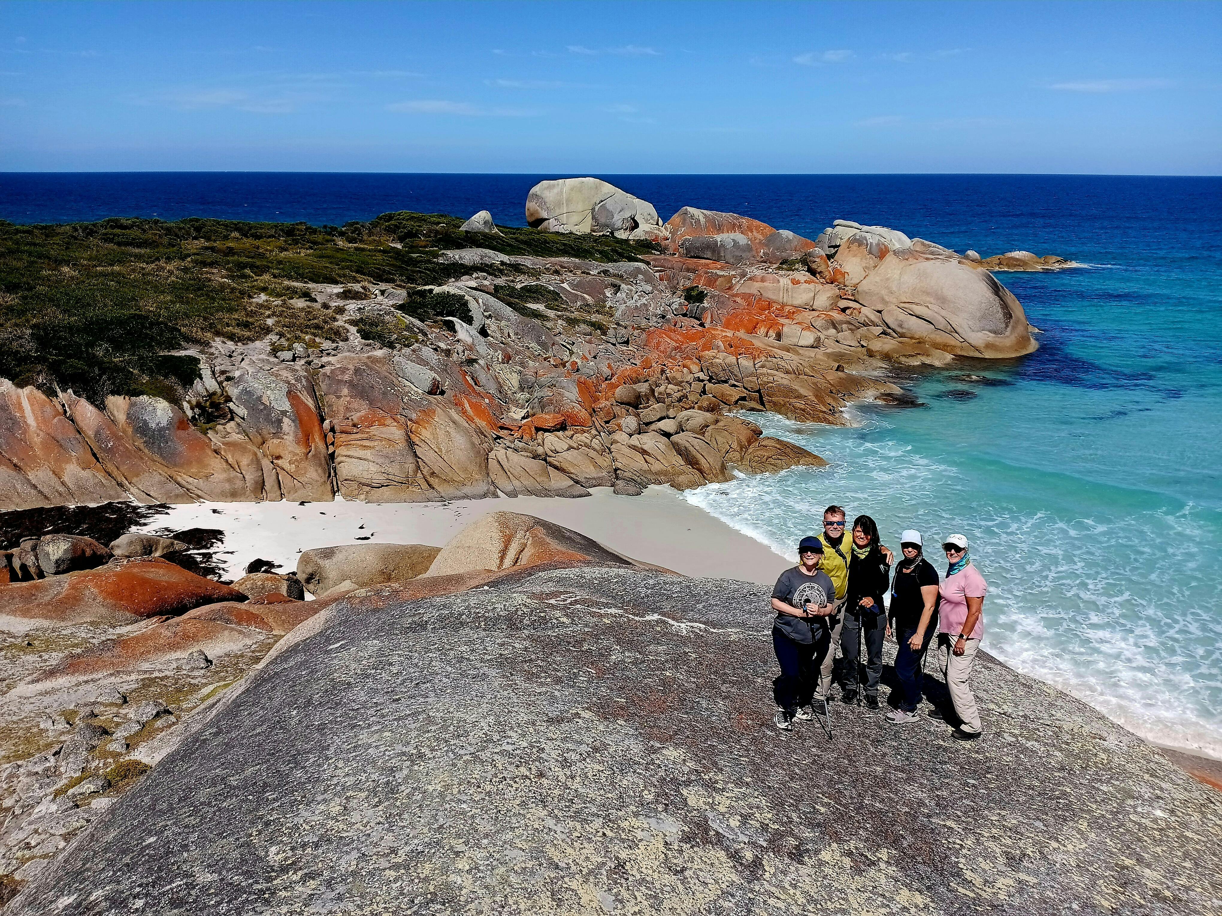Group of walkers standing on granite rocks overlooking the Bay of Fires coastline in Tasmania.