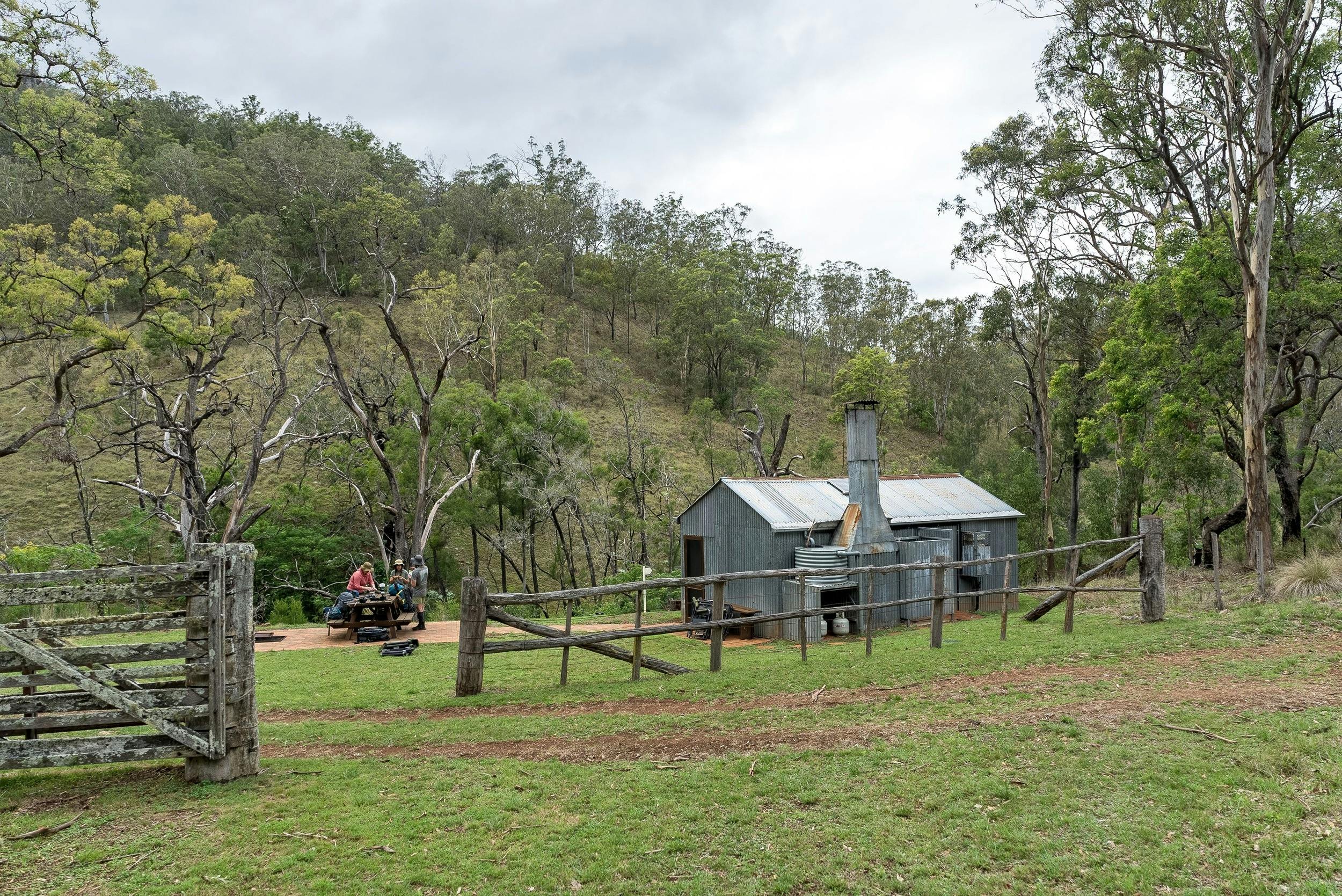 캠핑객들이 그린 굴리 트랙의 유산 오두막 밖에 앉아 있습니다.