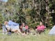Group of people sitting beside tent in grassy clearing