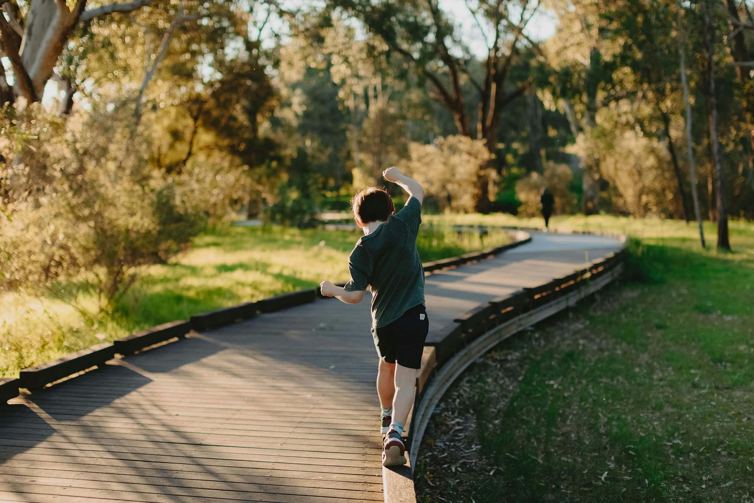 young child balanging on the edge of the wooden walking trail surrounded by greenery