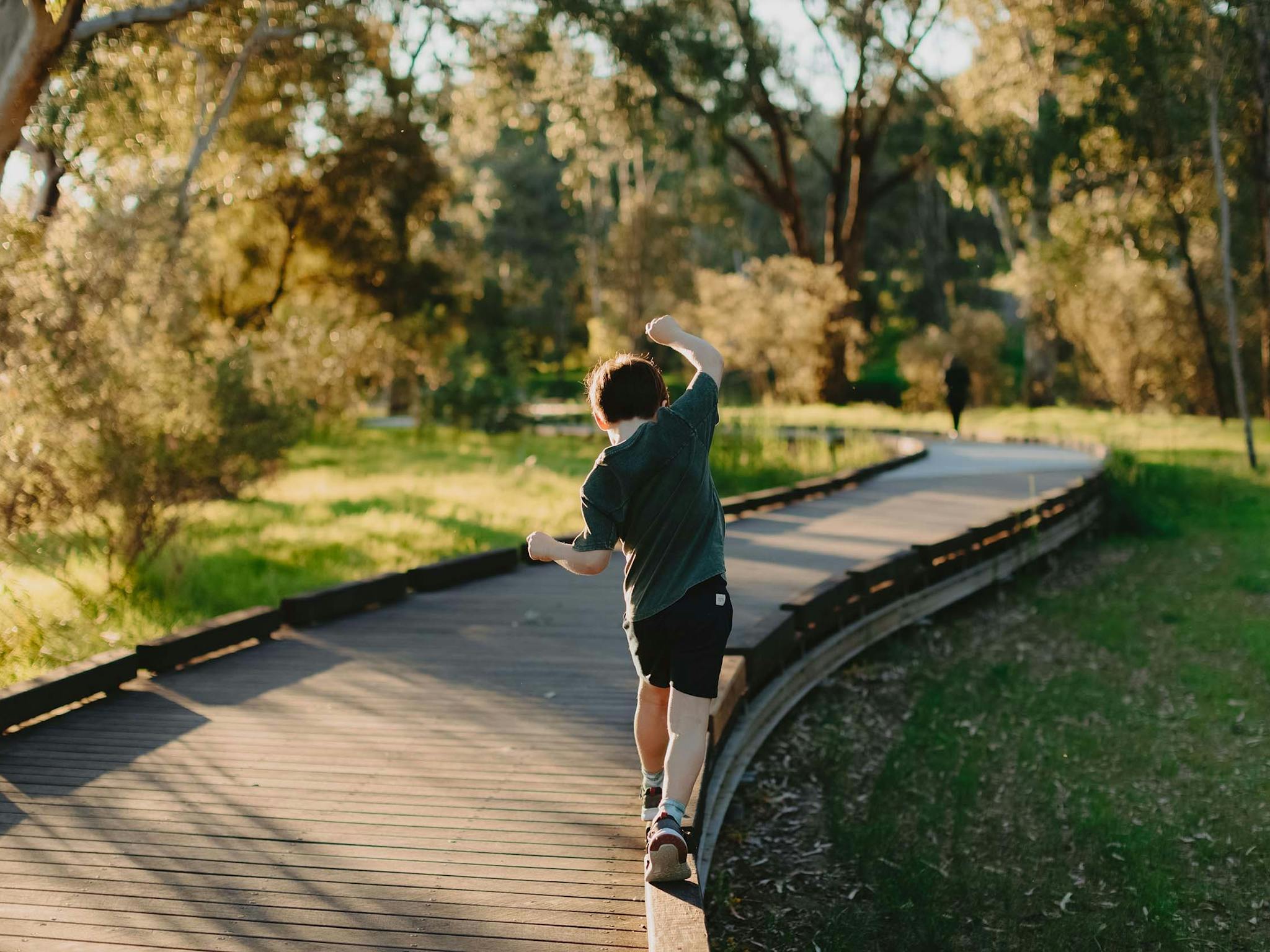 young child balanging on the edge of the wooden walking trail surrounded by greenery