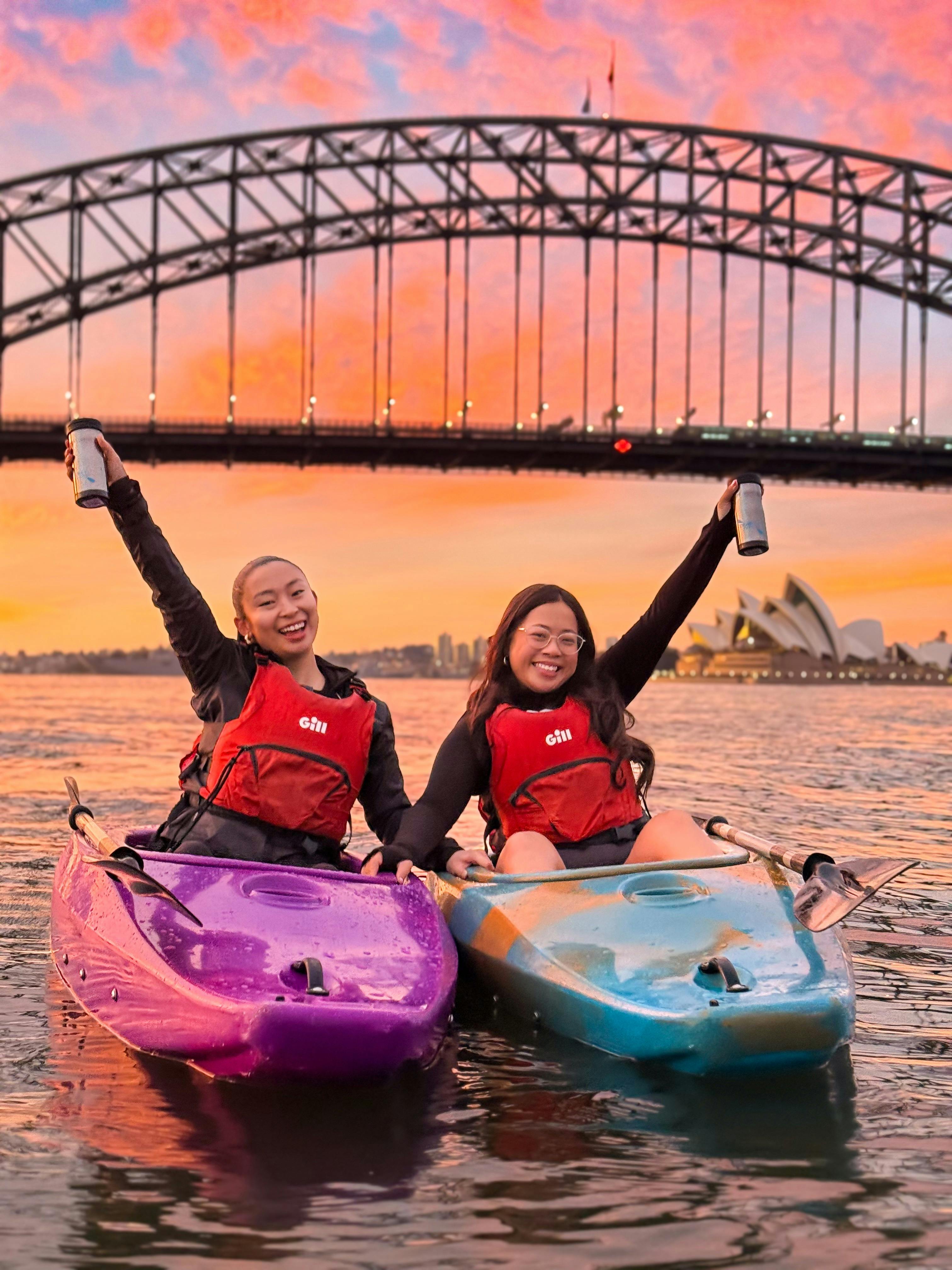 シドニー港のオレンジとピンクの美しい日の出を眺めながらコーヒーカップを掲げる女性 2 人。