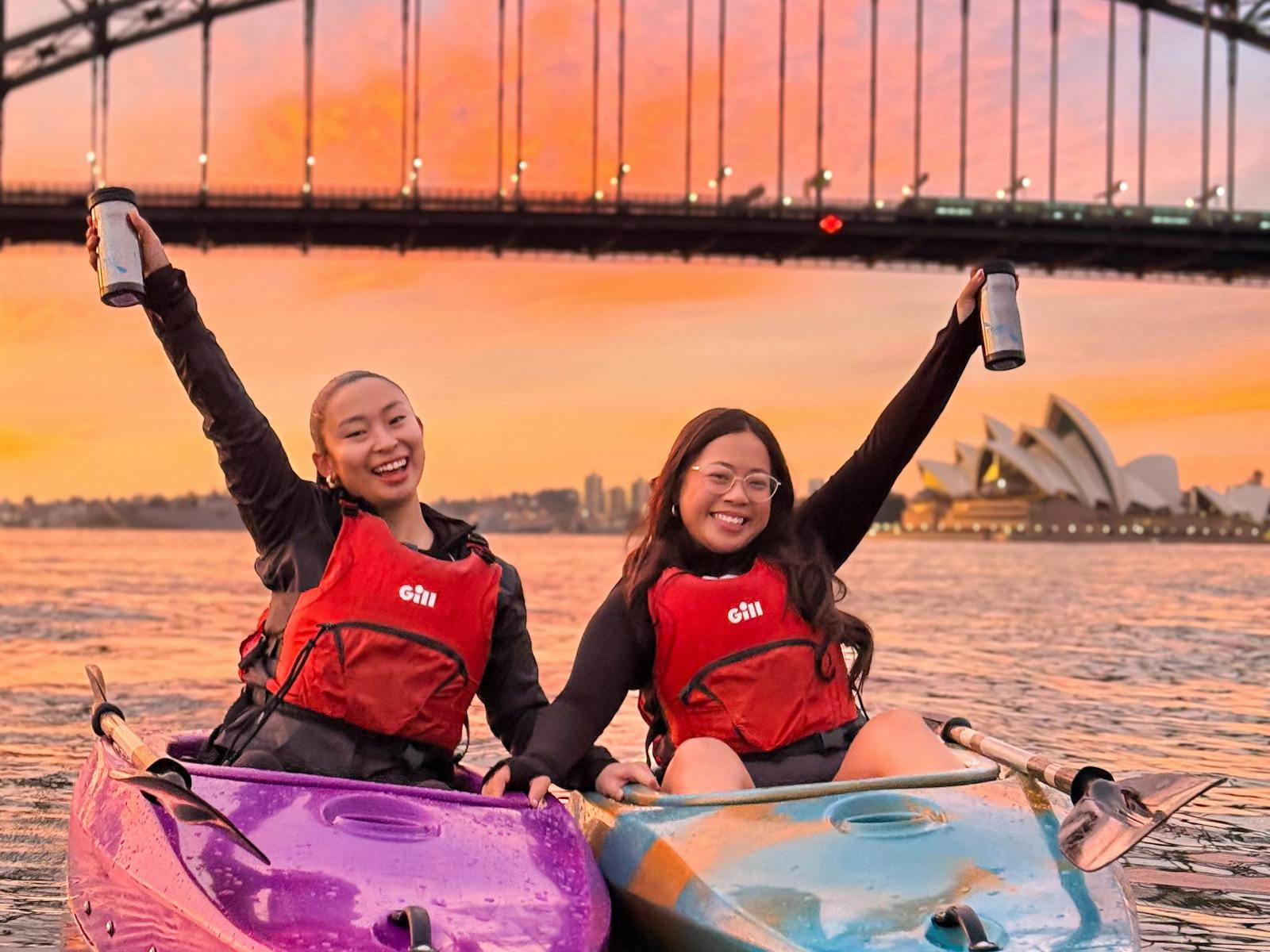 Two ladies raising their coffee cups with a stunning orange and pink sunrise over Sydney Harbour.