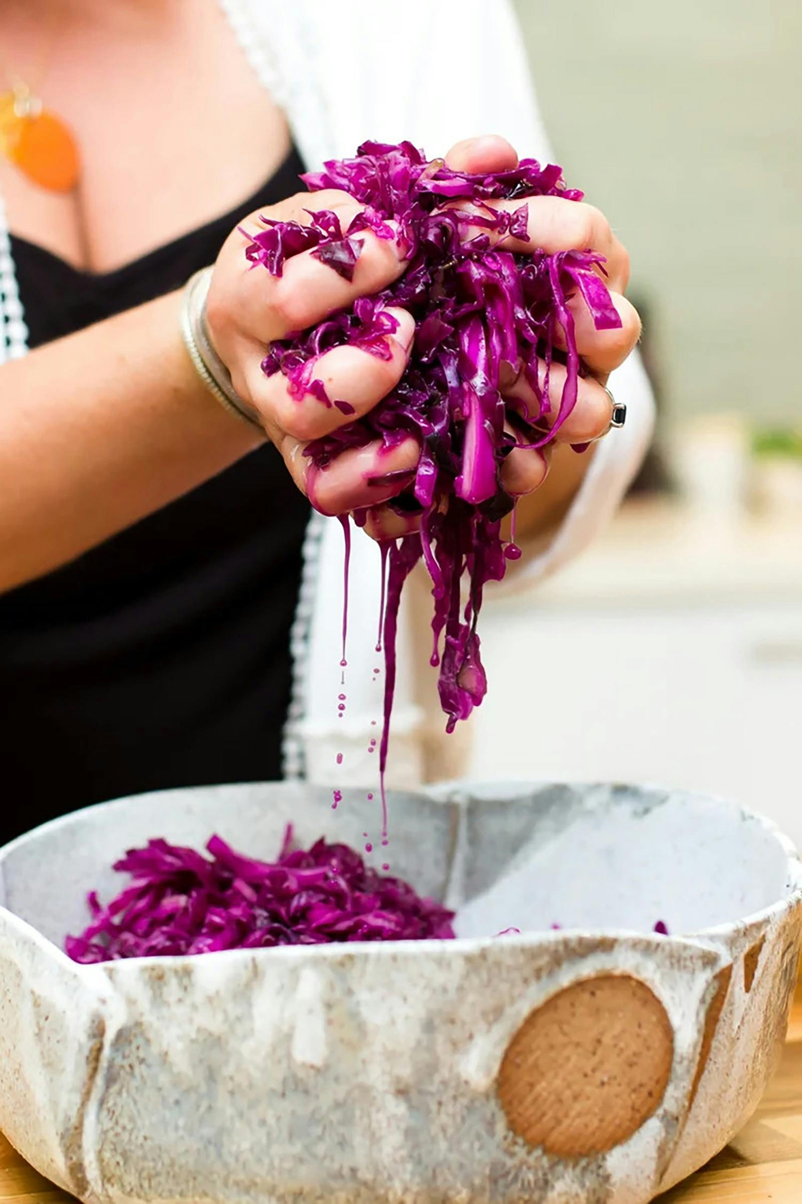 Hands holding shredded beetroot over a white bowl