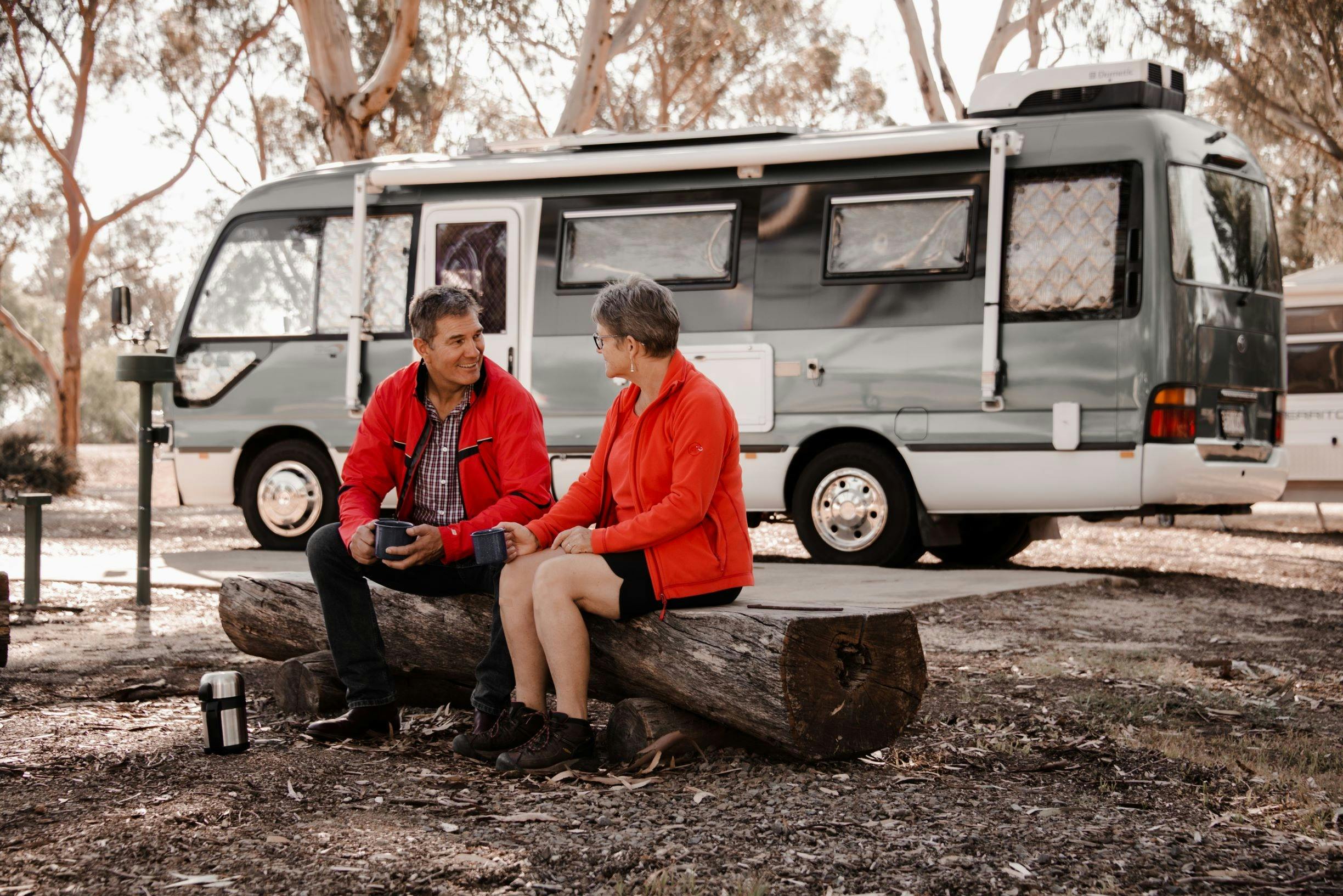 middle age couple sitting on a log in front of the camper van at a local caravan park
