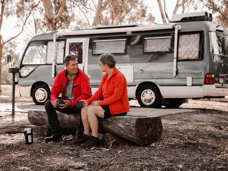 middle age couple sitting on a log in front of the camper van at a local caravan park