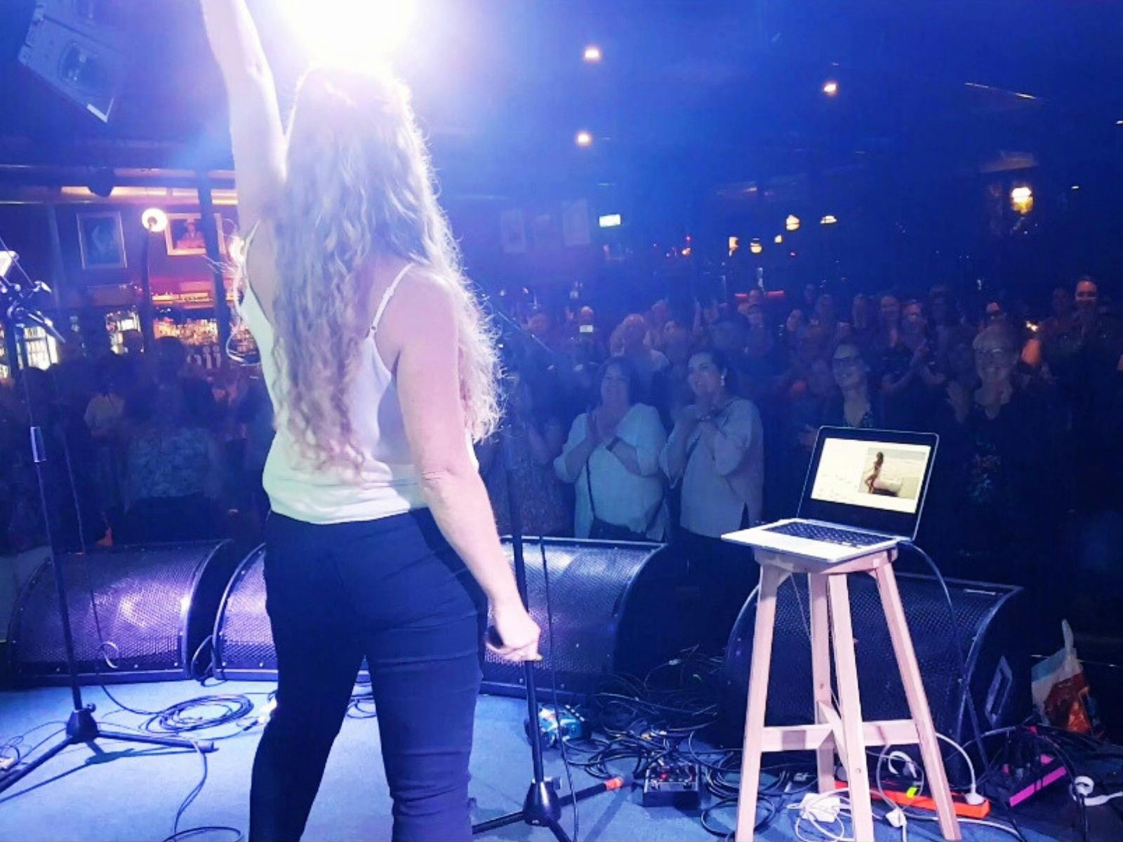 A woman stands on stage under spotlight with her fist in the air