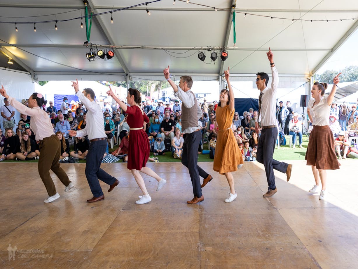 7 people dressed in bring colours perform a dance for a crowd