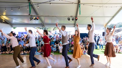 7 people dressed in bring colours perform a dance for a crowd