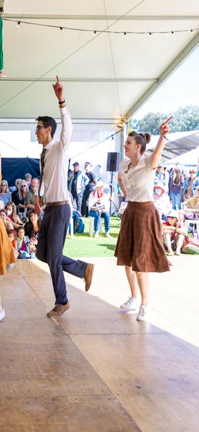 7 people dressed in bring colours perform a dance for a crowd