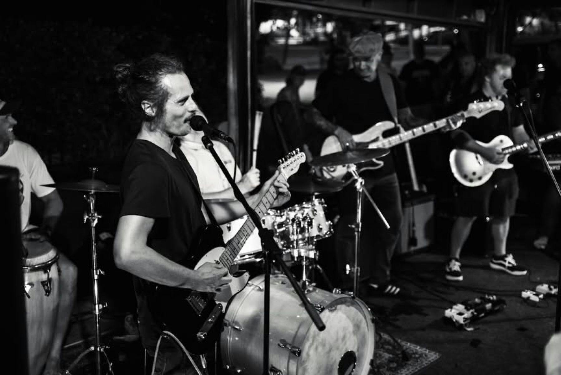 black and white image of man playing guitar in front of band