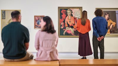 Visitors look at painted portraits in a Gallery; in the foreground, a couple sits together.
