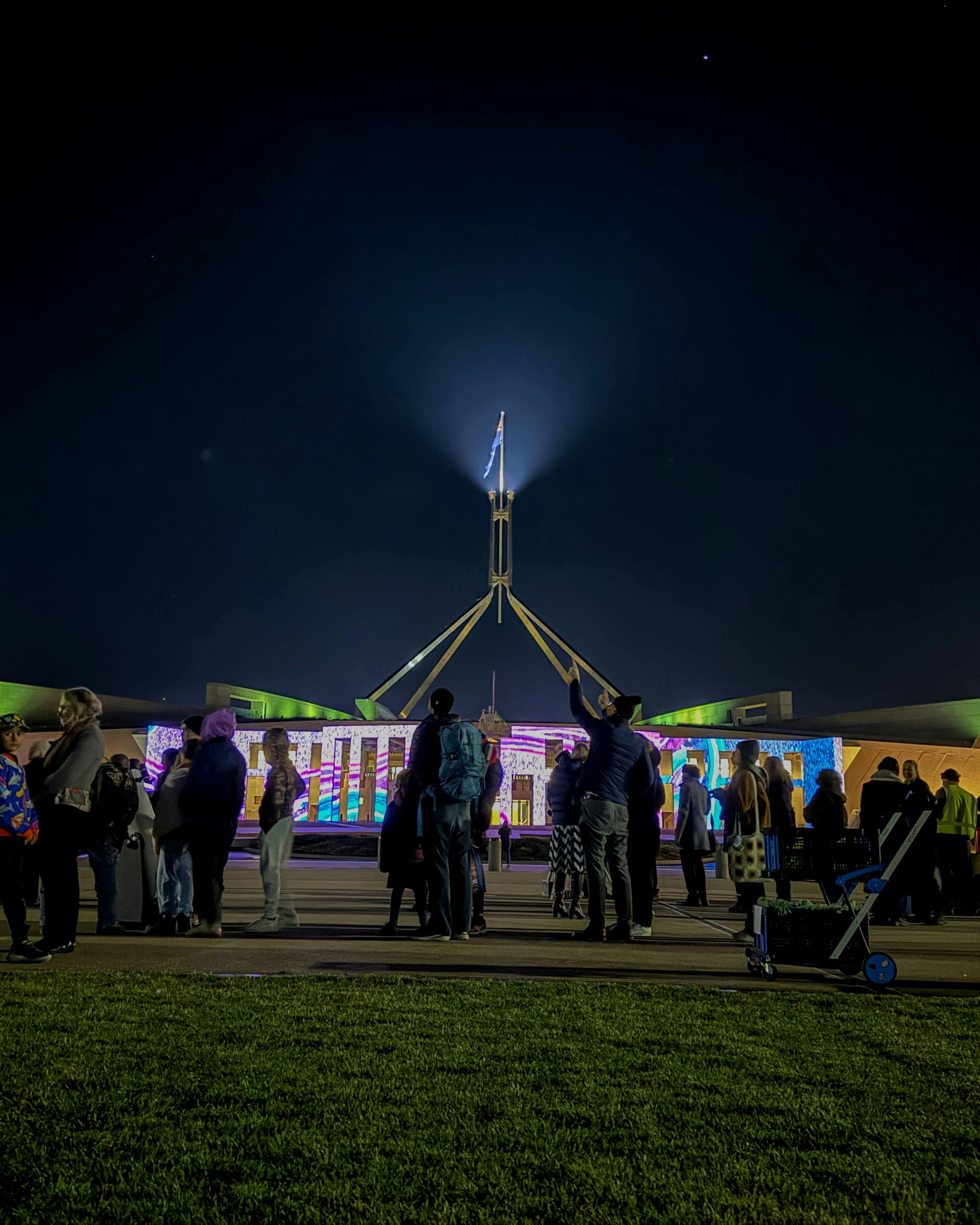 Night-time view of Australian Parliament House with the illuminated flag mast rising into a dark sky