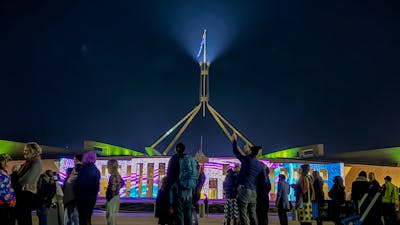 Night-time view of Australian Parliament House with the illuminated flag mast rising into a dark sky